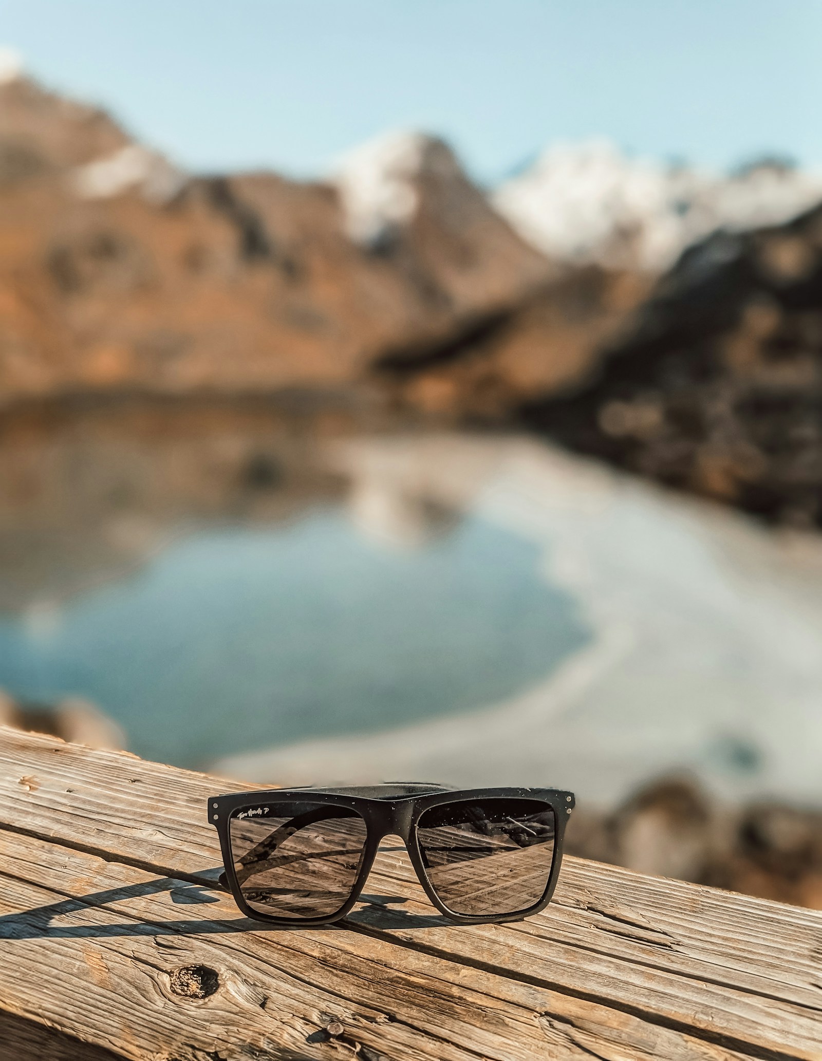 Sunglasses resting on a wooden railing overlooking a mountain lake, representing polarized glare reduction